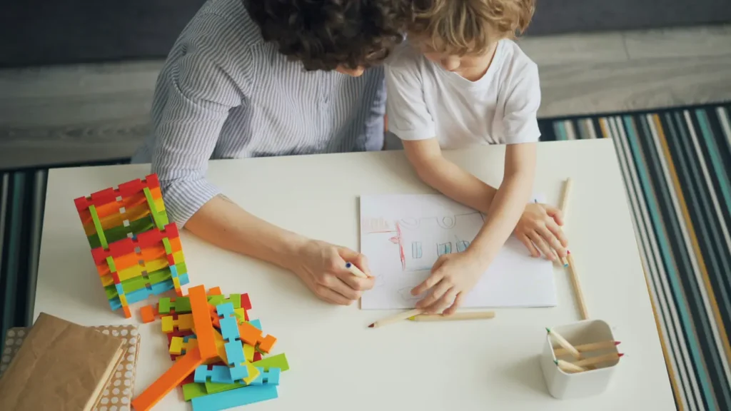 An adult and a child drawing together at a table, seen from above